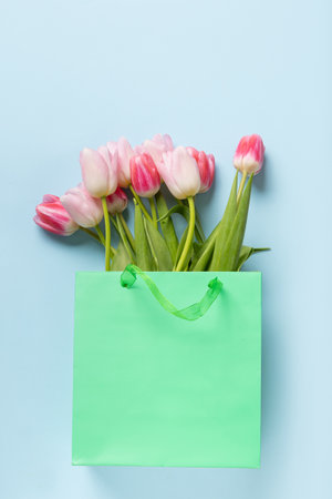 Fresh pink tulips in green paper bag on blue. Top view. Mothers day. Concept flowers delivery.の写真素材