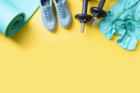 Sport and fitness green equipment, mat, dumbbells, fitness shoes on yellow. View from above, copy space.の写真素材