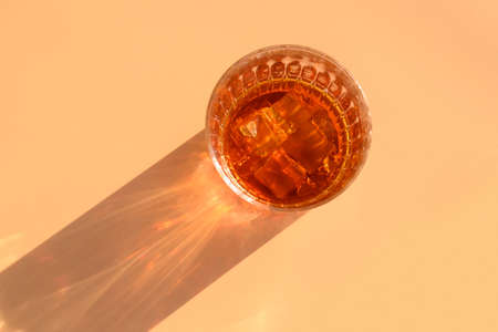 Glass of whiskey with ice cubes on beige background and sunny shadow. View from aboveの写真素材