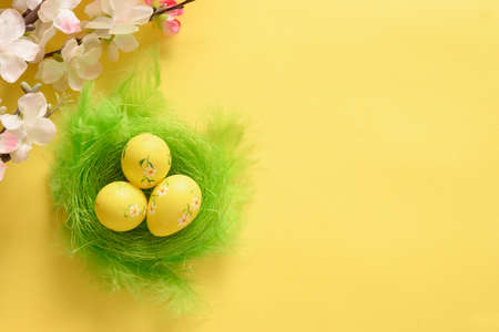 Quail easter eggs in nest and spring blomming flowers on yellow. View from above. Space for text.