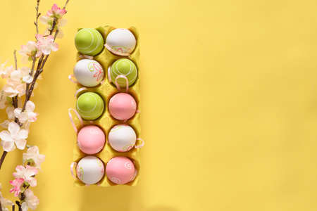 Easter pastel eggs in yellow carton box and spring blooming flowers on yellow. View from above. Space for text.の写真素材