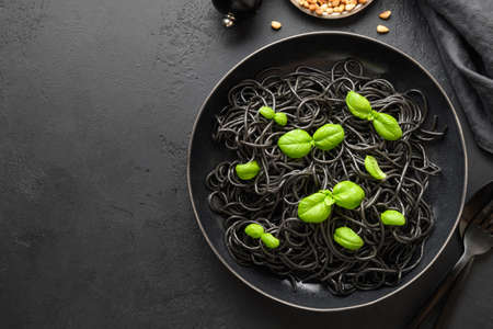 Black pasta spaghetti squid Ink decorated basil leaves on black background. View from above. Copy space.の写真素材