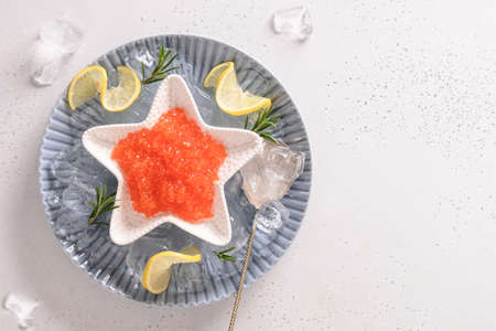 Red caviar in bowl in shape of star served with lemon and ice cubes on white table. Space for text. View from above.の写真素材