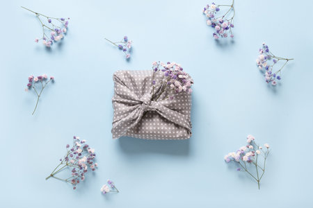 Spring eco-friendly gift wrapped in textile with fresh flowers on blue background. Sustainable gift. Traditional Japanese Furoshiki style. View from above.の写真素材