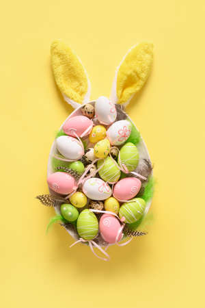 Easter painted eggs in plate as egg and bunny ears on yellow. Vertical greeting card. View from...