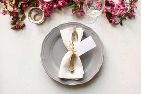 Elegance spring table setting with blooming apple flowers on white table. Top view. Festive dinner.