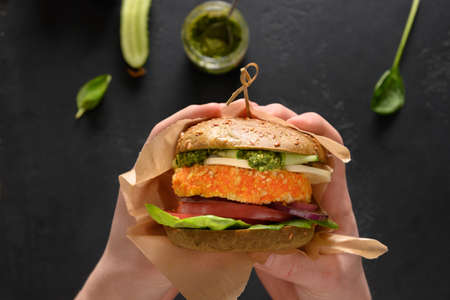 Vegan Burger of green spirulina buns, vegetables, vegan cheese, pesto carrot meatball in hands.の写真素材