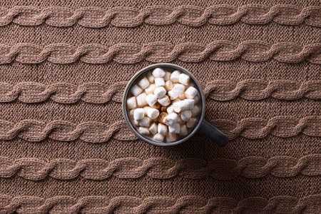 Cup of coffee or cocoa with marshmallow in cozy lifestyle warming scarf on brown background.の写真素材