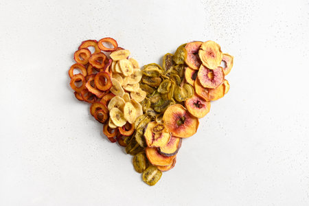 Heart made of dried sliced plums, kiwi, peach chips on white.の写真素材