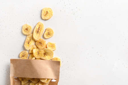 Dried sliced fruits banana chips in paper bag on white. Snack vegan sugarfree food.の写真素材
