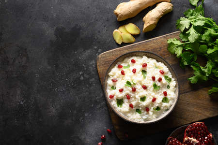 Curd Rice with pomegranate, cilantro, mustard seeds, ginger on a black background. Indian cuisine