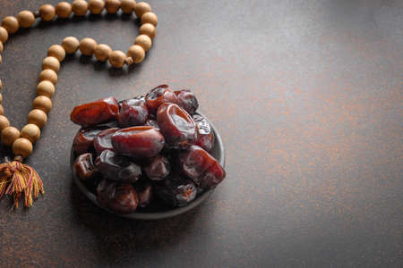 Ramadan. Wooden prayer beads and dates in bowl on brown. Eid Mubarak. Religious tradition.
