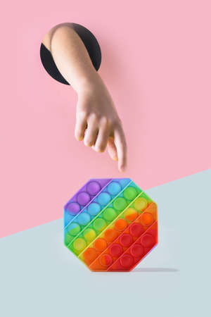Childs hand through hole in pink paper reaches for toy.