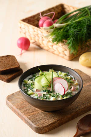 Homemade summer Okroshka soup with kefir served with rye bread and fresh vegetables on wooden table. Close up. Vertical format. Traditional Okroshka soup is Russian and Ukrainian cuisine for summer day lunch or dinner.の写真素材