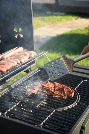 Beef steaks and sausages on grill. Barbecue backyard party. Outdoors.