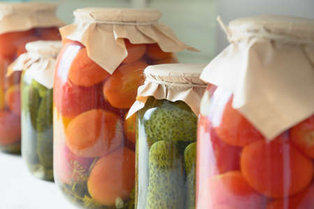 Homemade different canned food, marinated tomatoes, cucumber on storage shelf.
