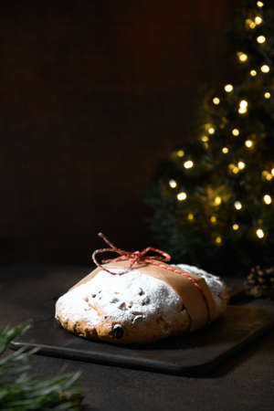 Traditional stollen decorated holiday rope on dark festive table with Christmas tree.の写真素材