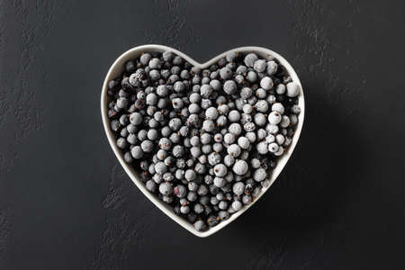 Frozen black currant in plate shaped as heart on a black background. View from above.の写真素材