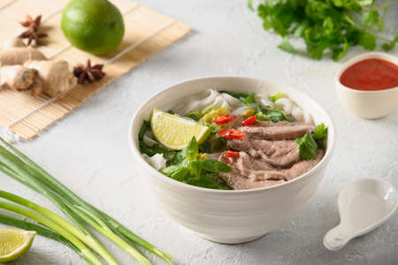 Pho Bo Soup with beef in white bowl on light backgound. Vietnamese cuisine.