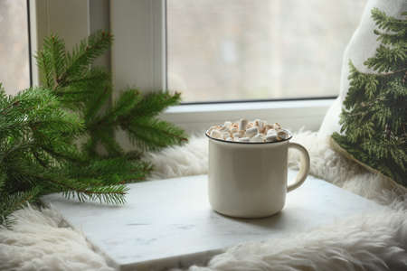 Winter coffee with marshmallow on cozy window sill with Christmas fir branches.