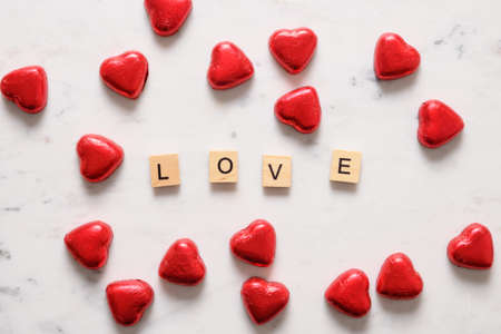 Valentine day chocolate sweets as heart in red foil and text - Love on white marble background.の写真素材