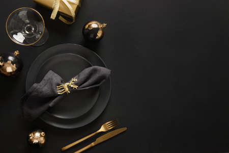 Christmas table setting with dark black plates, gold deer ring and gold cutlery. Golden gilded decorations.の写真素材