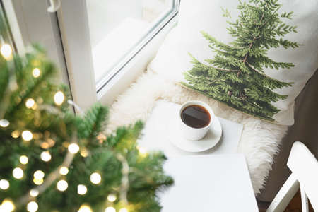 Winter coffee on window sill with Christmas tree and pillow for cozy reading.の写真素材