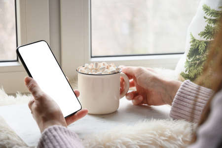 Woman drinking coffee and working in smartphone. Cozy winter holiday.