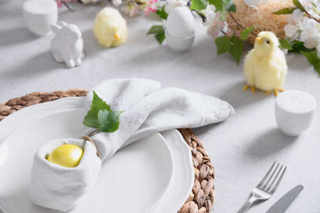 Easter table setting with yellow chick,decorations, fresh flowers and eggs. Elegance dinner at home.