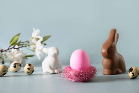 Easter pink egg and chocolate bunny in spring composition on blue.