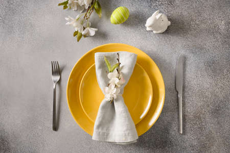 Easter festive table setting with yellow plate, spring flowers and green colorful eggs.