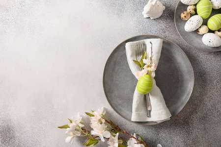 Easter festive table setting with gray plate, spring flowers and green colorful eggs.