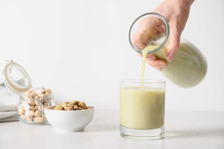 Woman pouring Pistachio milk in glass on white kitchen background. Lactose free. Vegan plant based milk.の写真素材