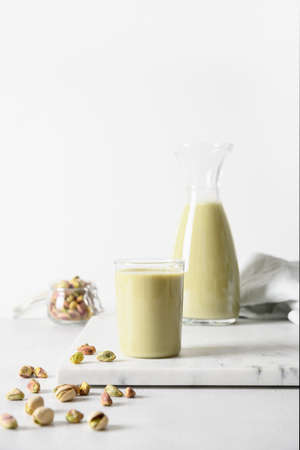 Pistachio milk in jug and pistachios on white background. Vegan plant based and lactose free milk. Vertical.の写真素材