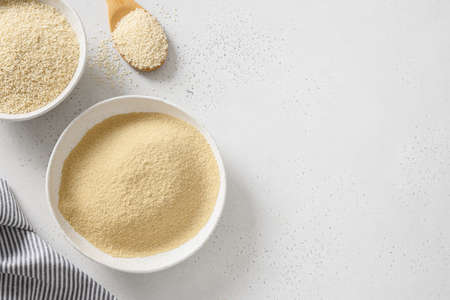 Sesame flour in bowl and white sesame seeds in wooden spoon on white background. View from above....