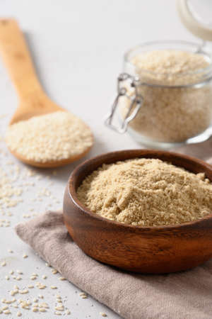 Sesame flour in wooden bowl and seeds in glass jar on white background. Vertical. Close up.の写真素材