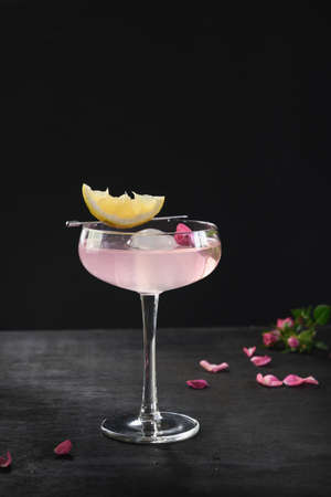 Freshness alcoholic cocktail with gin, rose flowers and lemon on black background. Freshness summer...