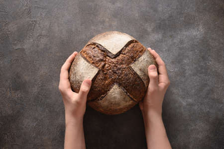Loaf of freshly baked bread with hemp flour in hands on gray background. Artisan bread. View from above.の写真素材