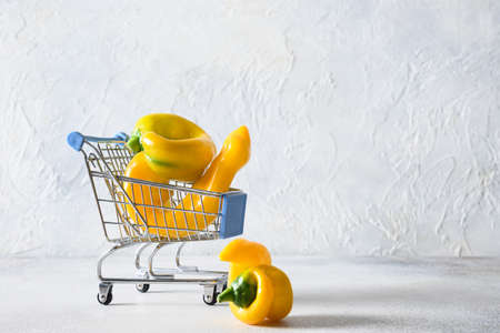 Shopping trolley full of fresh yellow pepper on gray background. Concept environmental vegan shopping. Organic food.の写真素材