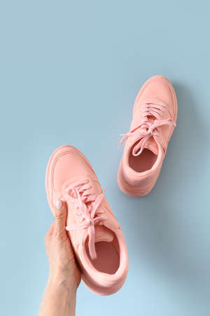 Pink female sneakers or sport shoes in womens hand on blue background. View from above. Vertical format.の写真素材