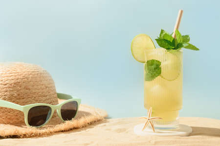 Freshness mojito cocktail on beach, straw hat and eyeglasses in sunny shadow. Concept of summer...
