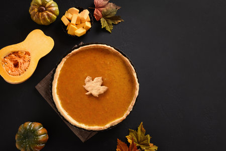 Homemade traditional Pumpkin pie with autumn leaves for Thanksgiving Day on black background. View from above. Flat lay. Copy space.の写真素材
