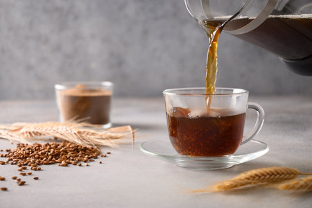 Pouring barley coffee in glass cup on gray background. Cooking healthy caffeine free alternative coffee. Close up.の写真素材