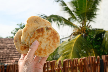 Authentic Sri Lankan three Pol Coconut Roti in hand against backdrop of tropical landscape....