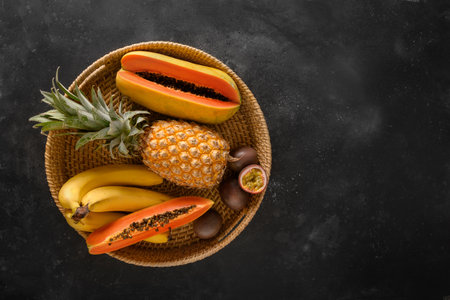 Popular Asian exotic fruits. Pineapple , passion fruit and papaya served in tray on black background. Top view, copoy space.の写真素材