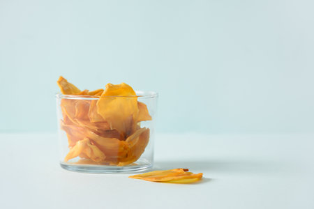 Organic jackfruit chips from tropical island Ceylon. Fruits chips in glass jar on blue background. Close up. Copy space.の写真素材