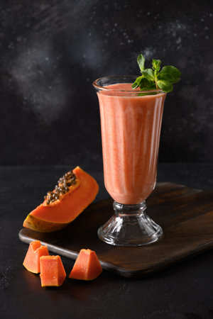 One glass of Papaya lassi on black background. Freshness cold beverage of yogurt, water, spices, fruits and ice. Popular beverage in India and Sri lanka. Vertical format.の写真素材