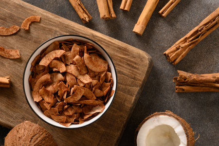 Coconut chips with cinnamon in bowl on brown background, home drying. Vegan and sugar free dessert. Top view. Sri lankan local snack.の写真素材