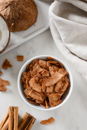 Coconut chips with cinnamon in glass jar on white background, home drying. Vegan and sugar free...