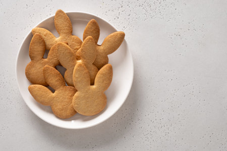 Easter cookies shaped of bunny in white plate on white background. View from above. Copy space. Festive food and kids snacks. Greeting card.の写真素材